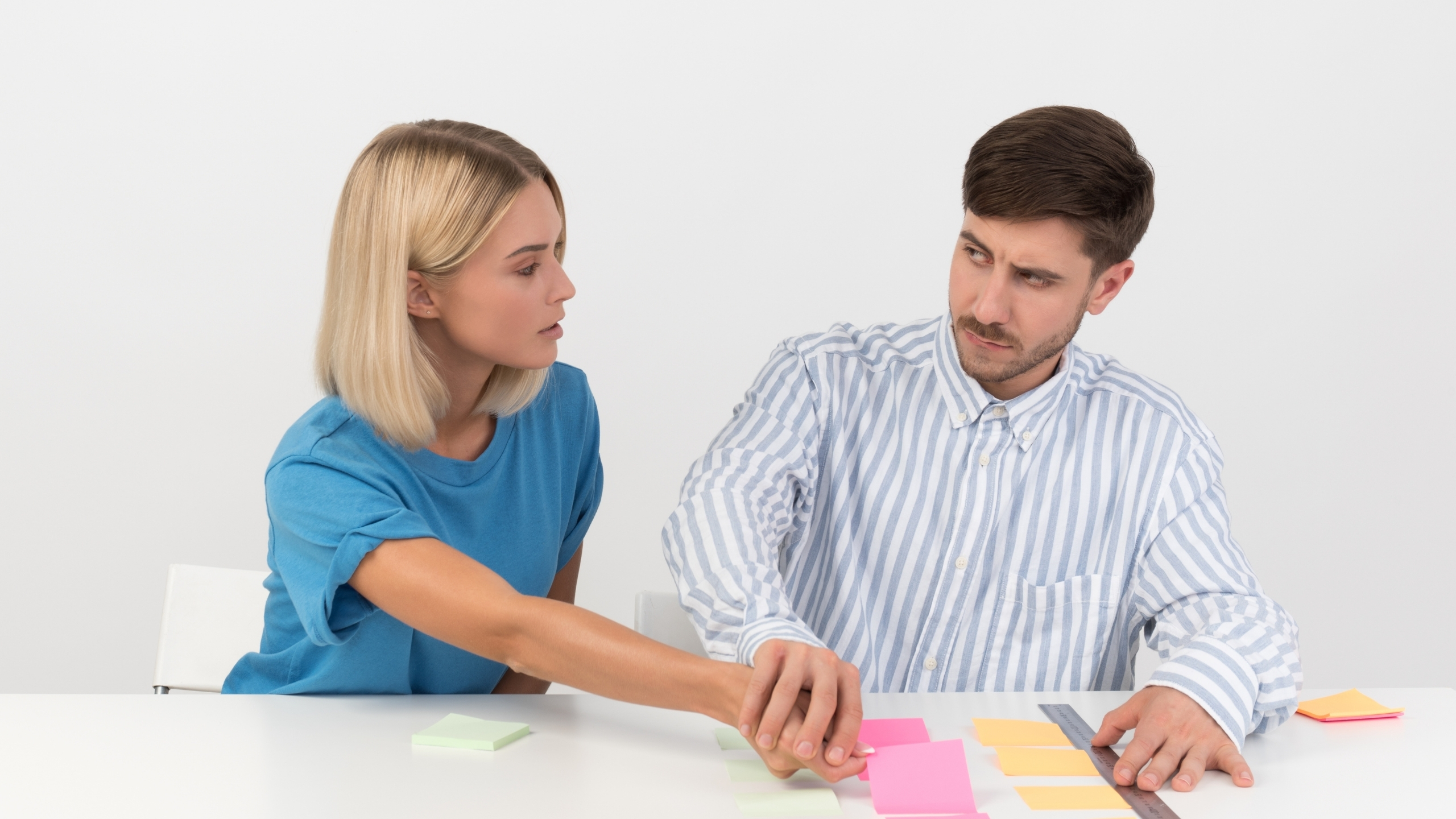 A man and woman are seated at a table, surrounded by sticky notes, actively discussing and organizing their ideas.
