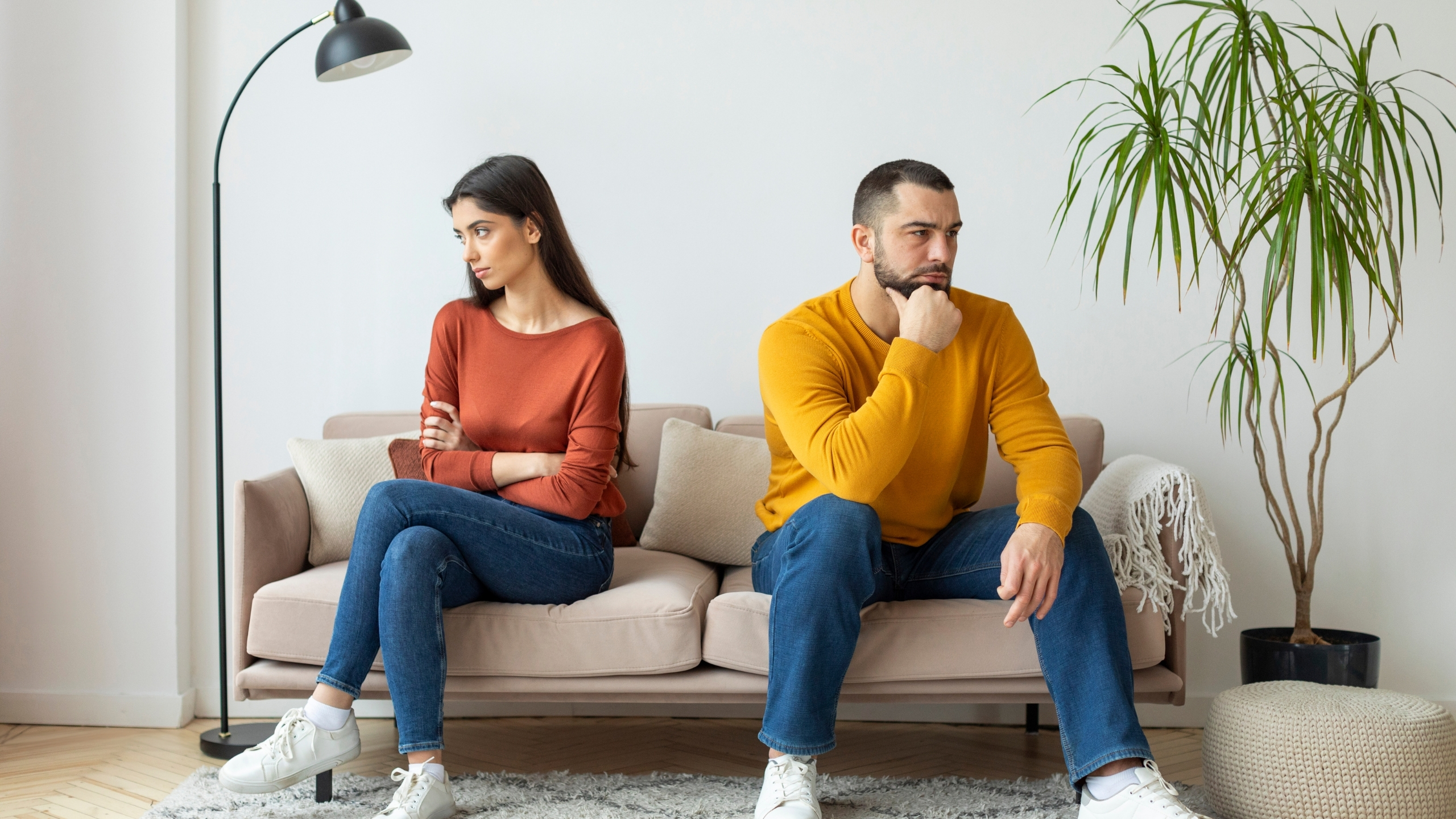 A man and woman are seated on a couch, appears to be distant from each other.
