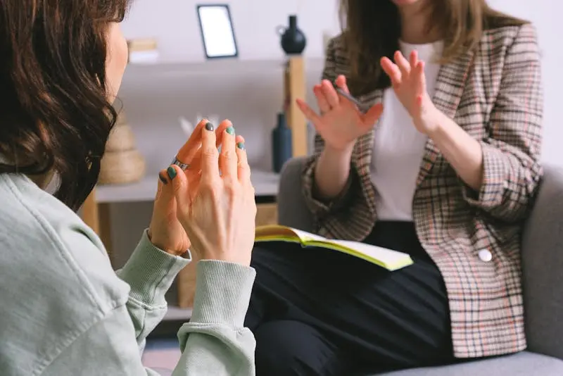 Two women seated in a chair, engaged in a conversation with friendly expressions.