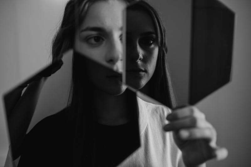 A woman holding a mirror and examining her reflection, representing common myths and misconceptions about schizophrenia.