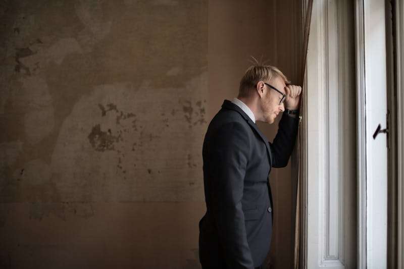 A man standing by a window with a thoughtful expression, representing symptoms of OCD and anxiety disorders.