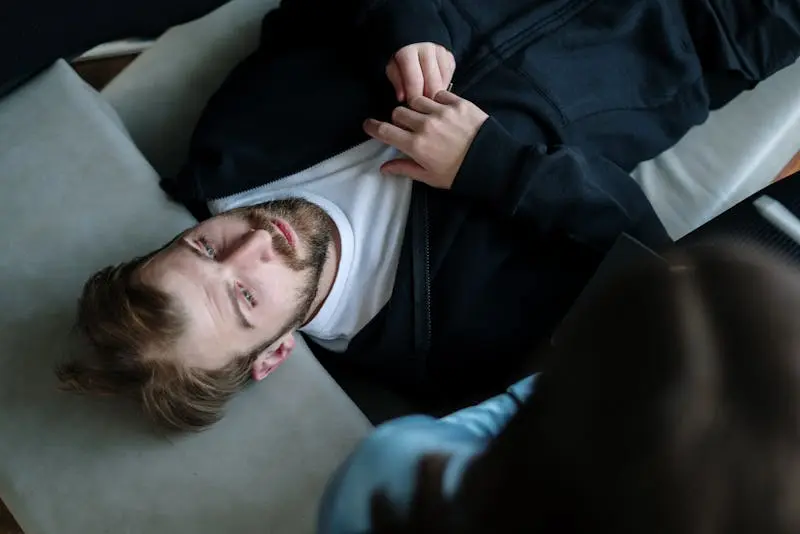 A man reclines on a couch, with his head resting on the floor, creating an unusual and relaxed posture.