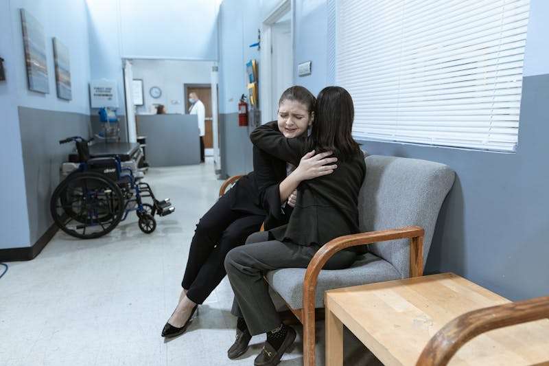 Two women sitting together in a hospital hallway, offering emotional support during a nervous breakdown recovery.