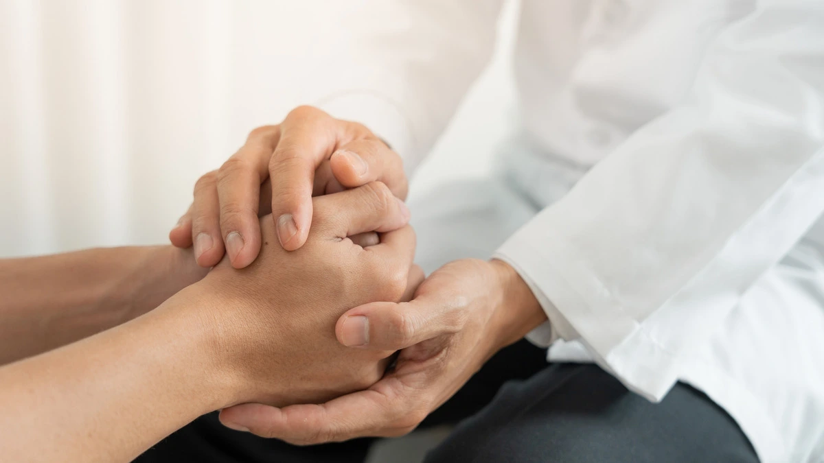 A doctor gently holds a patient's hand, conveying support and compassion during a medical consultation.